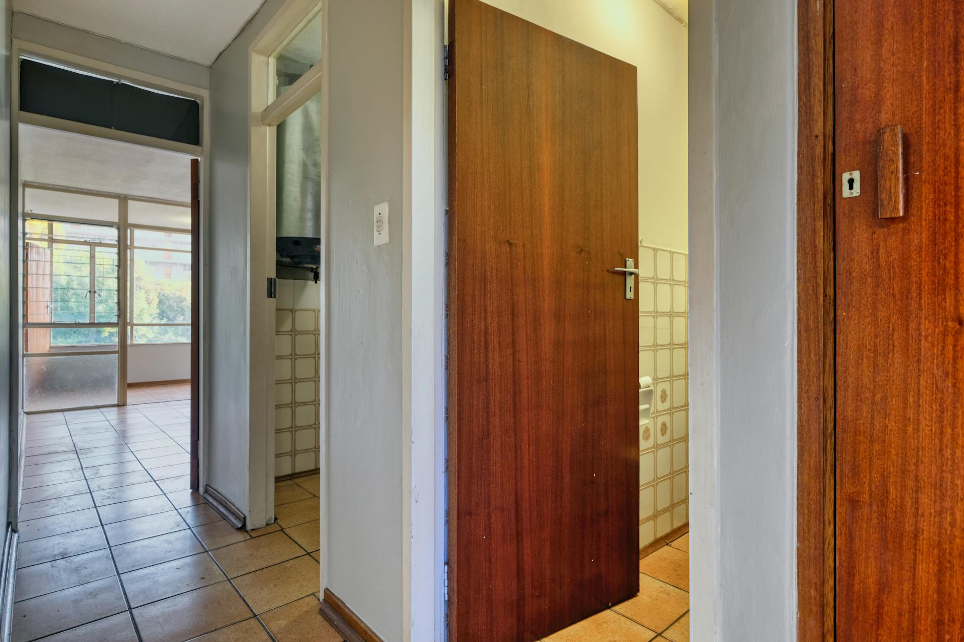 Jasny korytarz w mieszkaniu z drewnianymi drzwiami i jasną podłogą z płytek