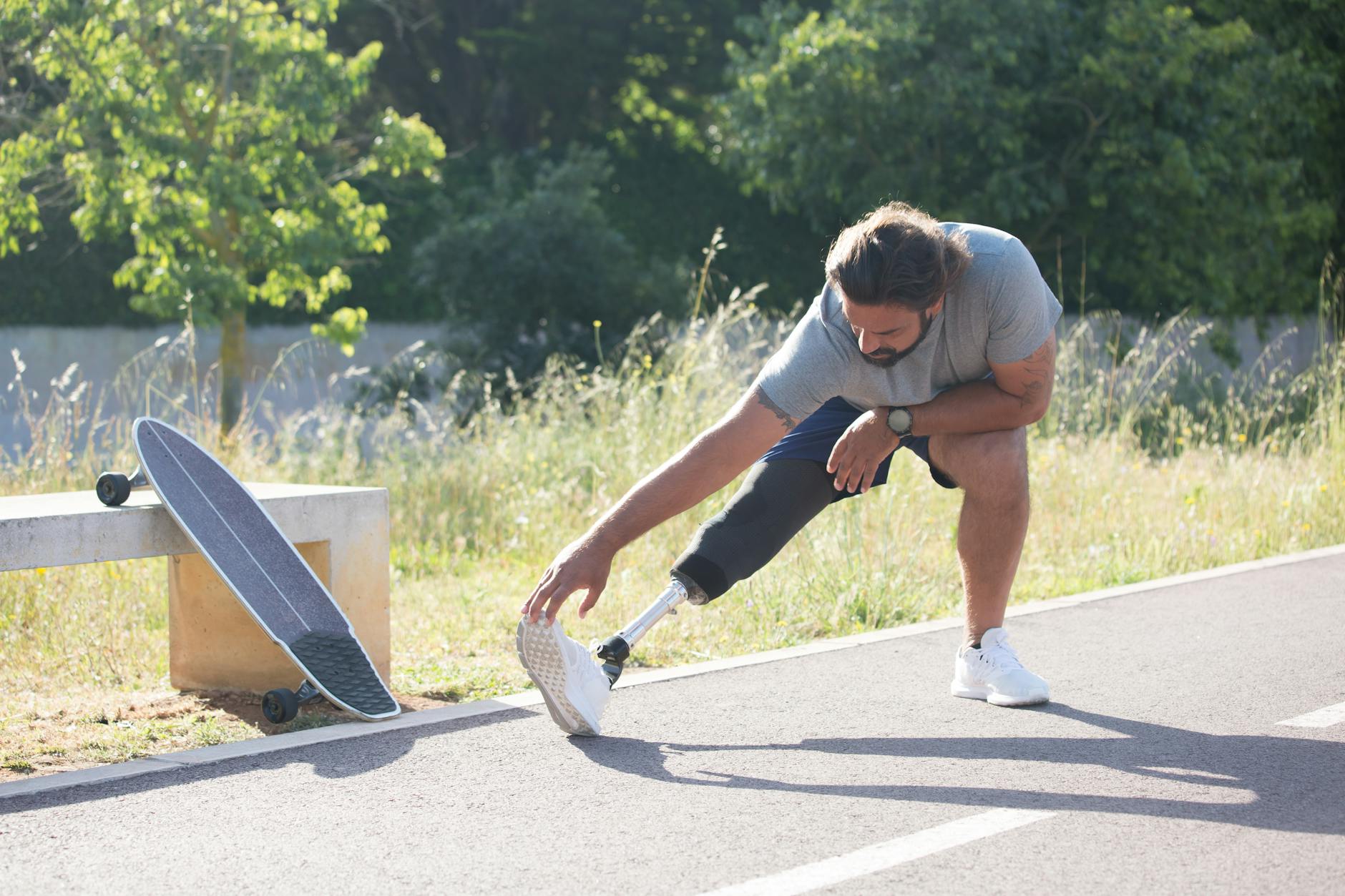 Mężczyzna z protezą nogi rozciąga się na ścieżce obok longboardu