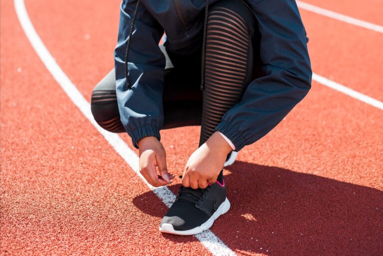 Sportowiec wiąże buty biegowe na bieżni podczas dnia