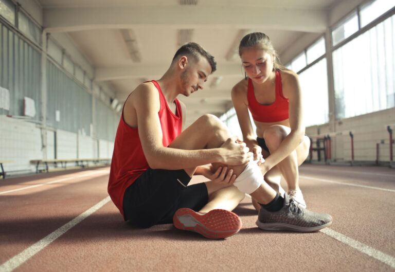 Sportsmenka bandażuje nogę kontuzjowanego zawodnika na bieżni sportowej